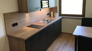 A modern kitchen with wooden cabinets, a built-in sink, and a window providing natural light. - Stan's Bed & Breakfast (Untergriesbach)
