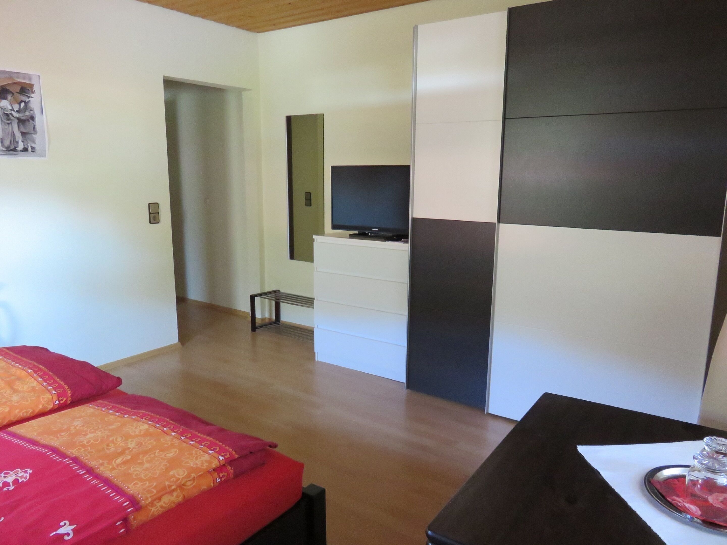 A modern room with a bed, a TV on a dresser, and a dining table with a glass.