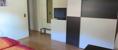 A modern room with a bed, a TV on a dresser, and a dining table with a glass.