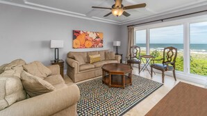 Una sala de estar con un sofá color beige, una mesa de centro y vista al océano a través de ventanas amplias.