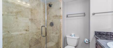A modern bathroom with a glass-enclosed shower, a toilet, and a marble countertop.