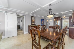 Un comedor espacioso con una gran mesa de madera y sillas, una araña y una cocina con armarios de madera oscura.