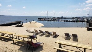 A beach with wooden picnic tables and lounge chairs, a pier with boats, and a clear sky. - Water-view in Kingsmill, 10 minutes to Busch Gardens & Colonial Williamsburg! (Williamsburg)