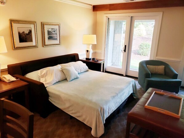 A hotel room with a bed, bedside table, lamp, chair, and a sliding glass door leading to an outdoor area. - Water-view in Kingsmill, 10 minutes to Busch Gardens & Colonial Williamsburg! (Williamsburg)