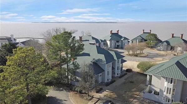 A residential area with multiple houses, a parking area, and a body of water in the background. - Water-view in Kingsmill, 10 minutes to Busch Gardens & Colonial Williamsburg! (Williamsburg)