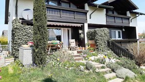A two-story house with a balcony, a garden with various plants, and a staircase leading to the upper floor. - Ferienwohnung Lucretia a3 (Ruhstorf)