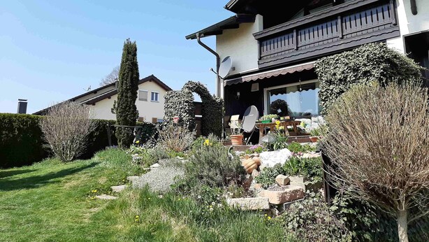 A two-story house with a balcony, surrounded by a garden with various plants and a lawn. - Ferienwohnung Lucretia a3 (Ruhstorf)