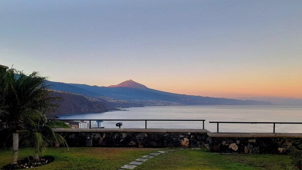 A coastal view with a stone pathway leading to a seating area overlooking the sea and a mountain. - The best views of the island of Tenerife (Juan Fernández)