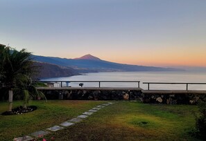 Une vue sur la côte, avec un sentier en pierre menant à un espace aménagé offrant une vue sur la mer et une montagne.