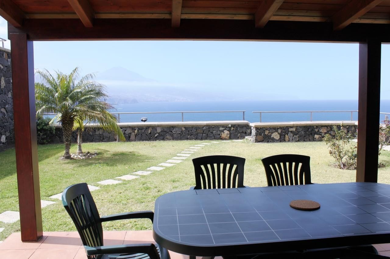 An outdoor patio with a table and chairs, a stone wall, and a view of the ocean.