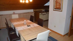 A compact kitchen with wooden cabinets, a dining table with chairs, and a hanging light fixture. - Ferienwohnung Stoiber (Frauenau)
