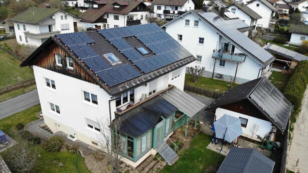 A two-story house with a sloped roof, solar panels, and a small attached garage. - Ferienwohnung Stoiber (Frauenau)