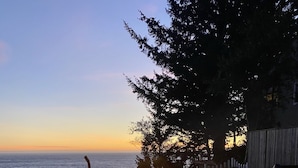 Una fogata con llamas, una silla y vista al océano al atardecer.