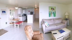 Una sala de estar con sofá, sillón, mesa de centro y televisor. Hay un comedor con mesa y sillas.