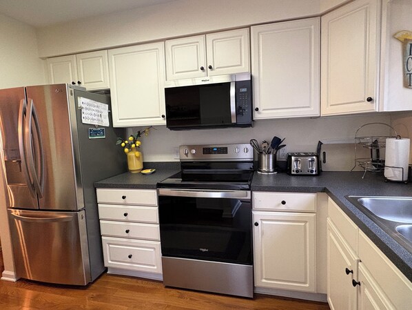 A modern kitchen with white cabinets, stainless steel appliances including a refrigerator, microwave, oven, and toaster, and a wooden floor. - Cozy, clean townhome. East Rte 1. Near historic Lewes, trails, 5 mins from beach (Lewes)