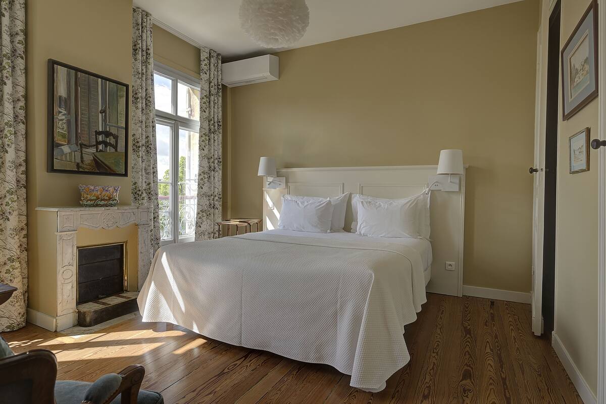 Une chambre à coucher avec un grand lit, une cheminée et une fenêtre avec des rideaux.
