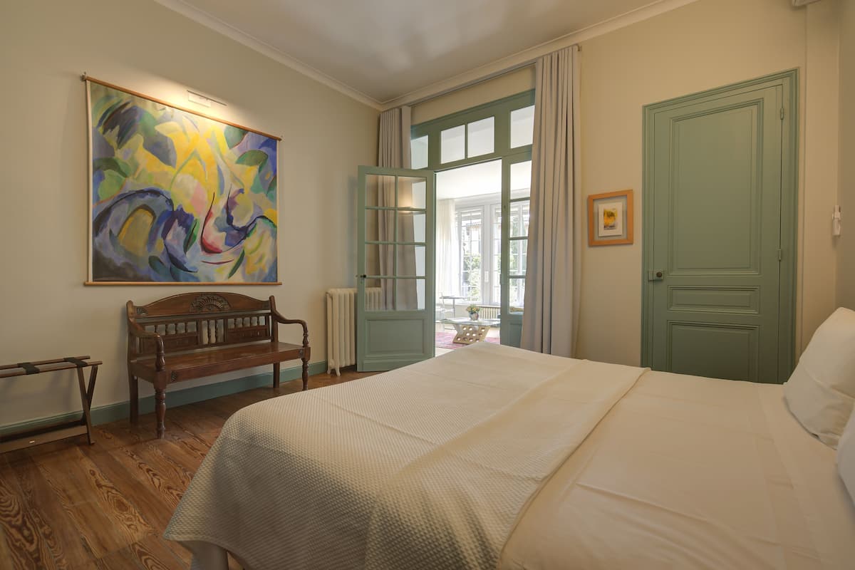 Une chambre à coucher avec un grand lit, un banc, un tableau et une porte avec une fenêtre.