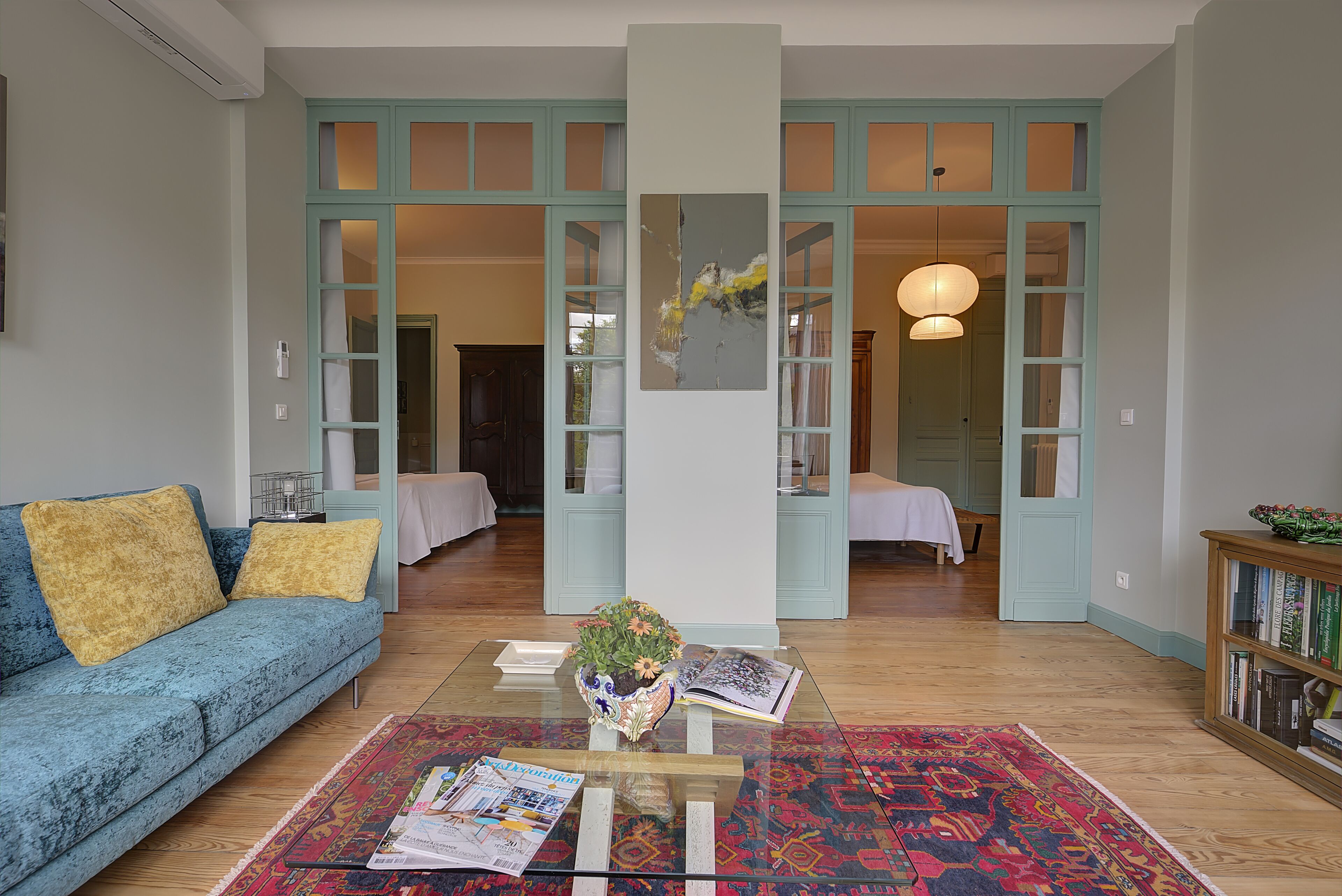 Un salon avec un canapé bleu, une table basse avec des magazines, un vase de fleurs et une bibliothèque.