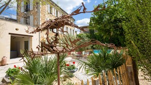 A courtyard with a metal sculpture, a pool, and a building with a balcony. - Clos d'Argenson (Bergerac)