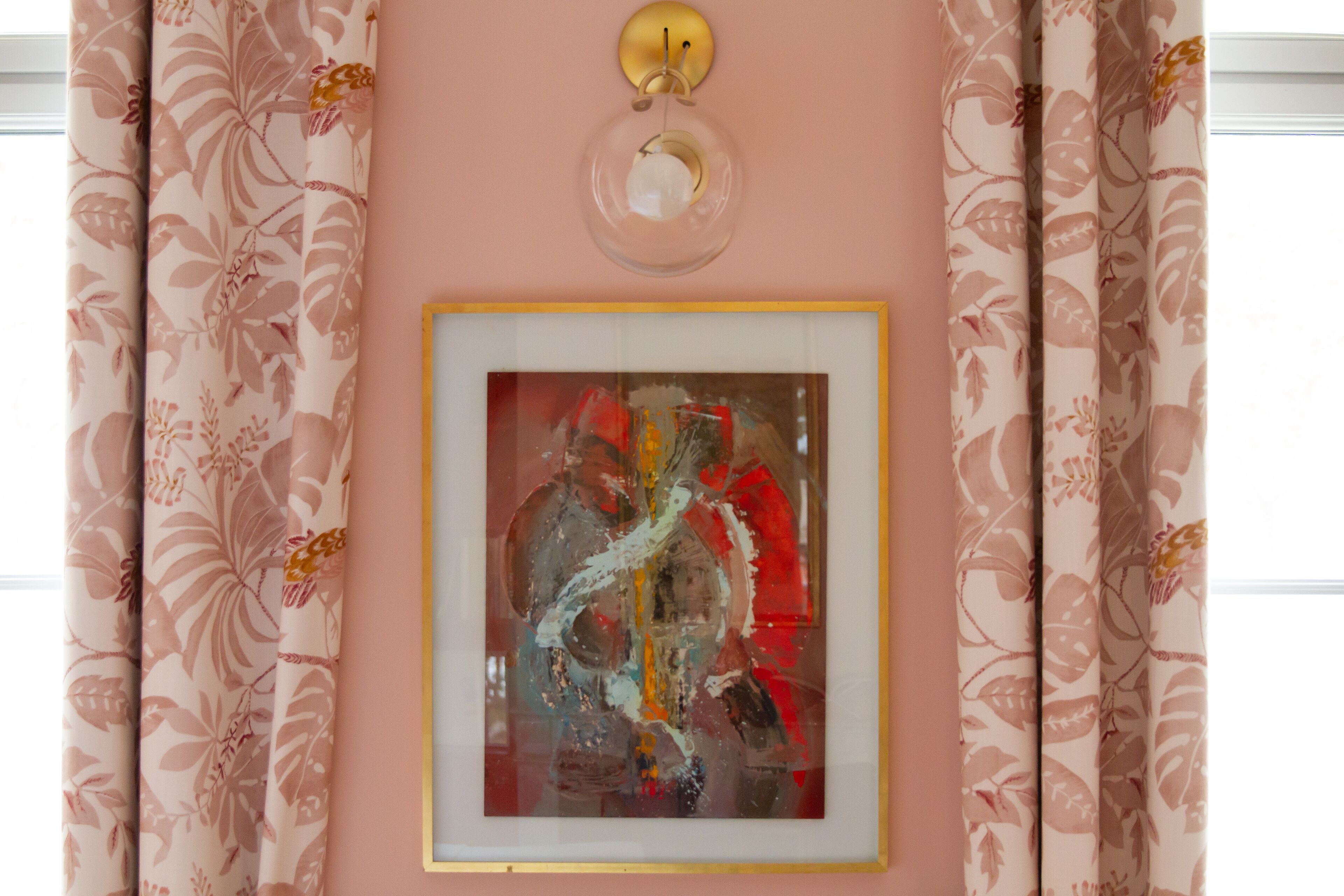 A framed abstract painting on a wall, surrounded by floral-patterned curtains.