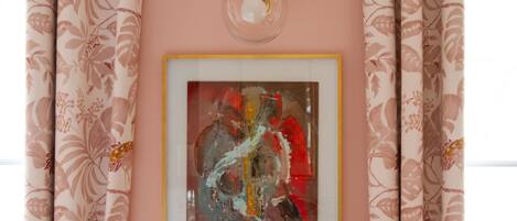 A framed abstract painting on a wall, surrounded by floral-patterned curtains.