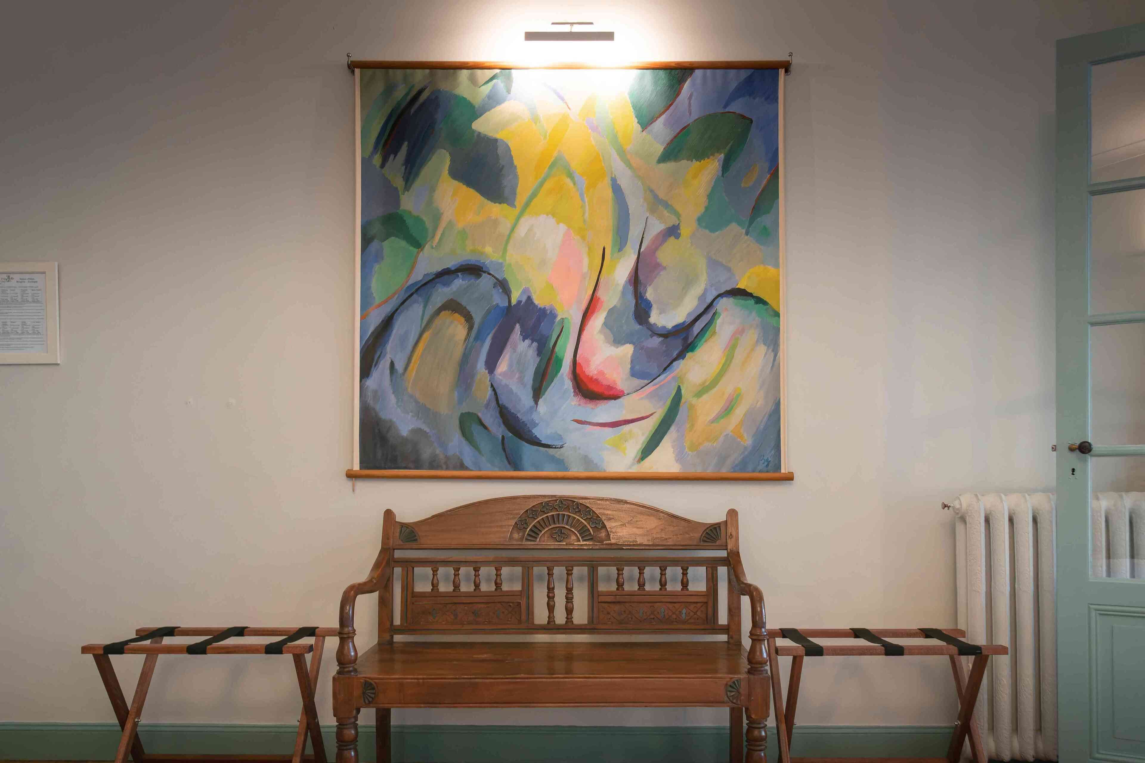 A room with a wooden bench, a radiator, and a colorful abstract painting on the wall.