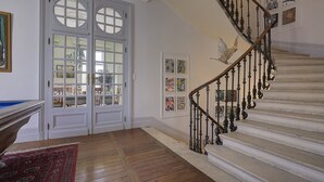 A staircase with ornate black balusters, a wooden floor, and a red rug leading to a door with glass panels. - Clos d'Argenson (Bergerac)