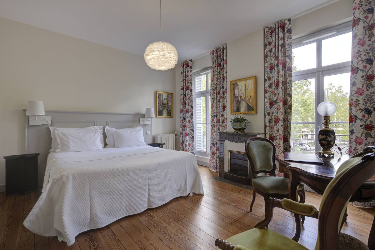Une chambre à coucher avec un grand lit, un bureau avec une lampe, une chaise et une cheminée.