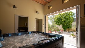 A hot tub in a room with a view of a garden and a door leading to another room. - Clos d'Argenson (Bergerac)
