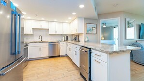 A modern kitchen with white cabinets, stainless steel appliances, and a marble countertop. - Phoenix VII 7508 | Luxury Gulf-Front Condo (Orange Beach)