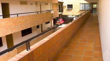 A corridor with tiled flooring, a red car parked in the background, and a sign for Los Cerezos Aparta Hotel.