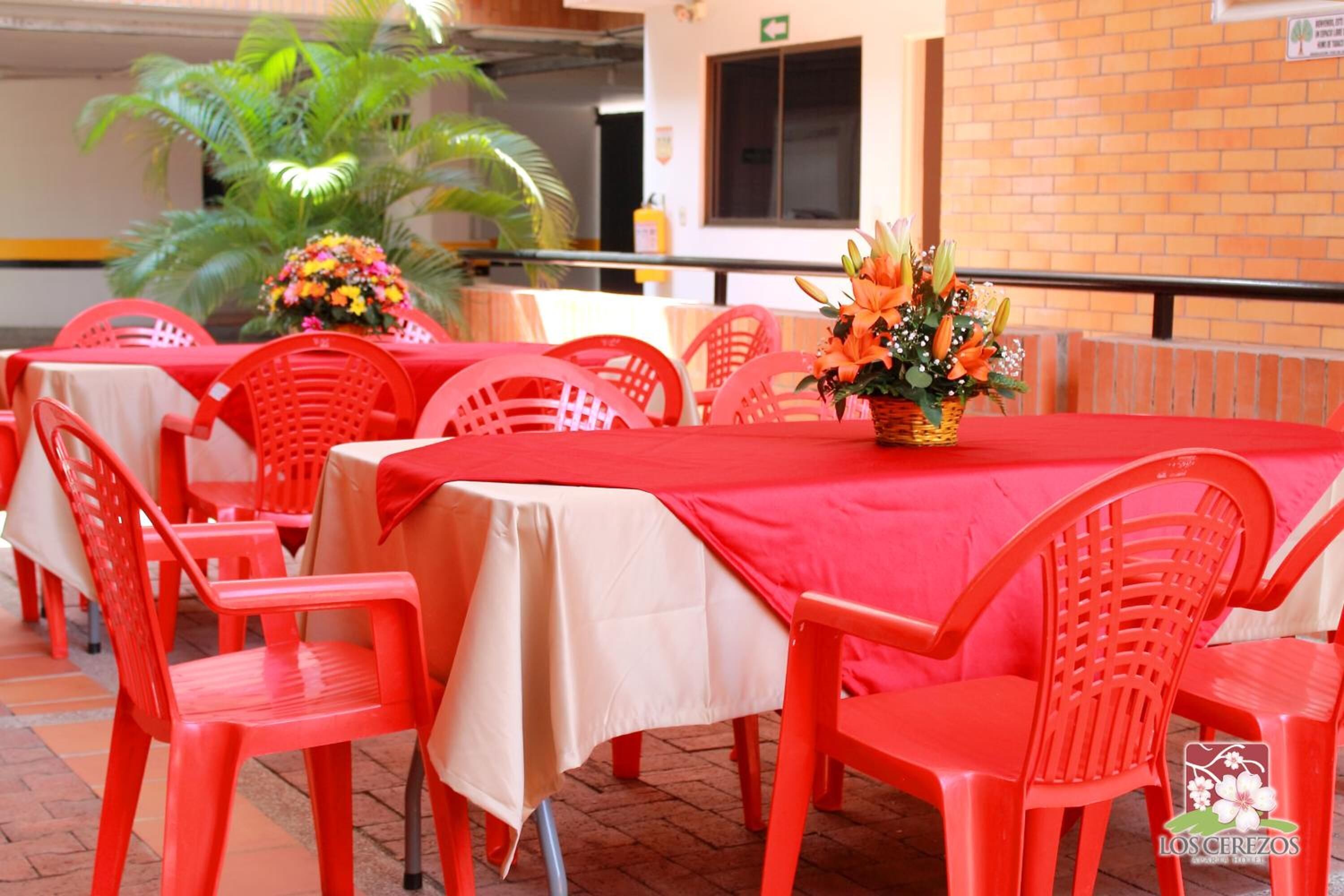 A dining area with red plastic chairs and tables, a potted plant, and a brick wall.