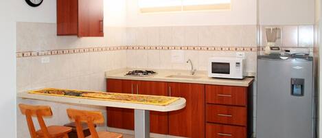 Una cocina con armarios de madera, microondas, refrigerador, lavamanos y un reloj en la pared.