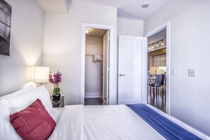 Hotelkamer met een bed, nachtkastje met lamp, vaas met bloemen en uitzicht op de badkamer en keuken.
