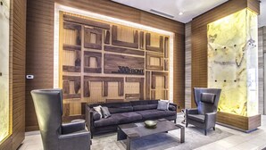 Eine moderne Lobby mit einem Ecksofa, zwei Sesseln, einem Couchtisch und einer Wanddeko mit geometrischem Muster und dem Text "300 FRONT".
