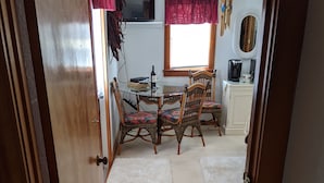A dining area with a glass table, wicker chairs, a red curtain, and a window with blinds. - Beautiful Ocean Front Studio with direct beach and access to a deck.  (Kill Devil Hills)
