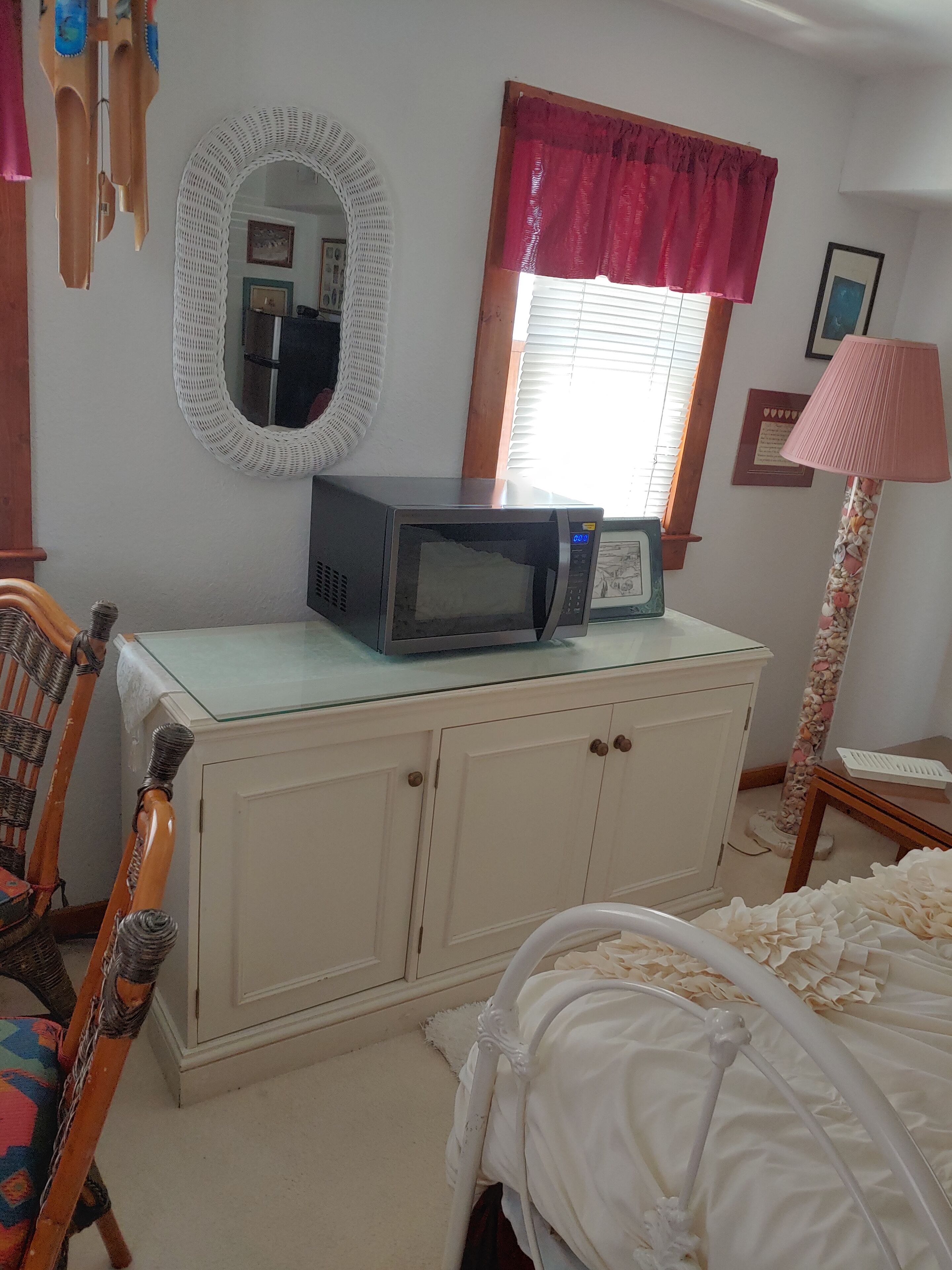 A bedroom with a bed, a dresser, a microwave, a mirror, a window with curtains, and a lamp.