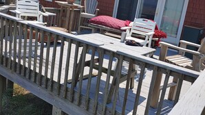 A wooden deck with outdoor furniture, including chairs and a table, overlooking a backyard with a brick house and a sliding glass door. - Beautiful Ocean Front Studio with direct beach and access to a deck.  (Kill Devil Hills)