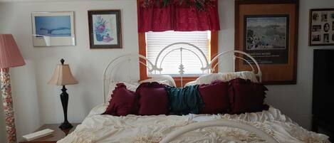 A bedroom with a metal bed frame, a window with blinds, and wall-mounted artwork.