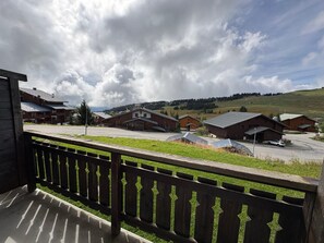 A wooden balcony overlooking a village with traditional buildings and a grassy field.