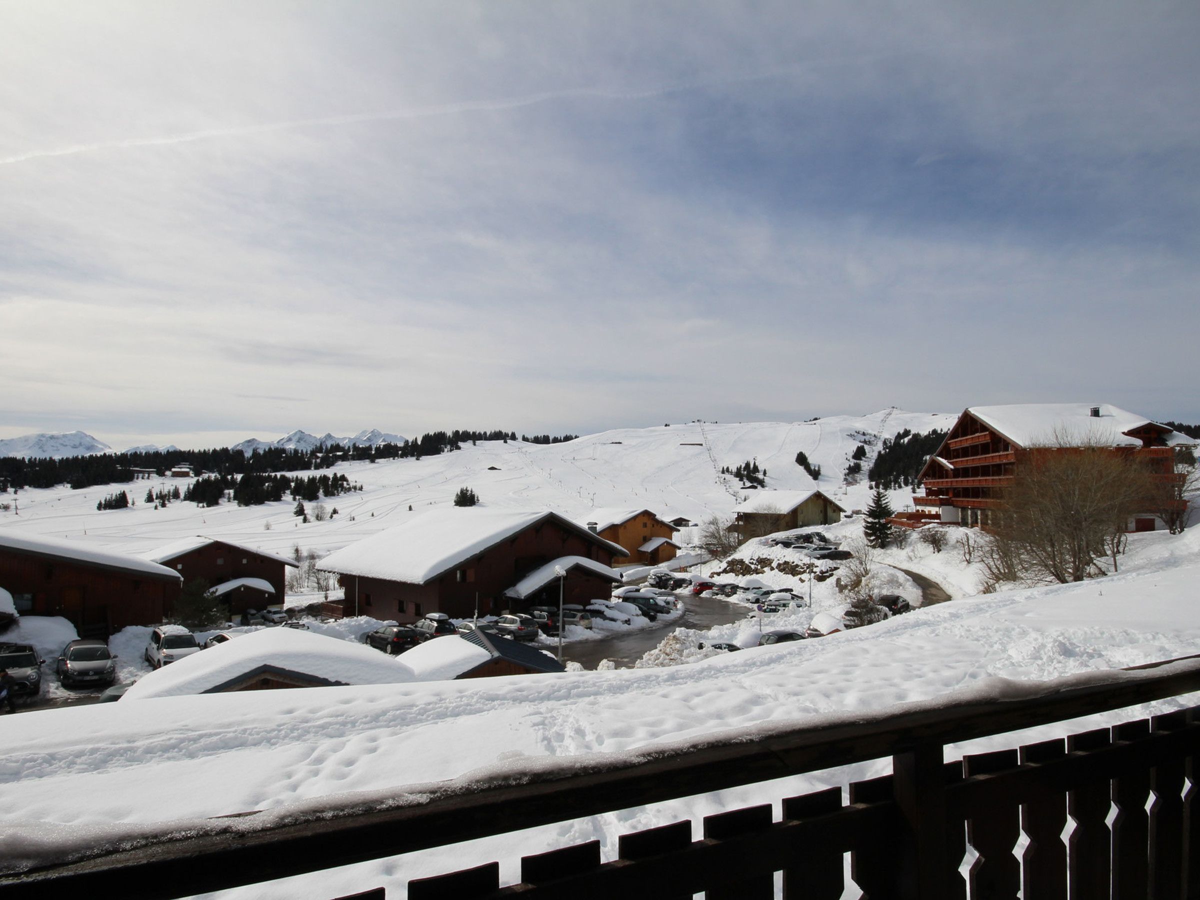 A snow-covered village with traditional wooden buildings, a ski slope in the background, and a clear sky.