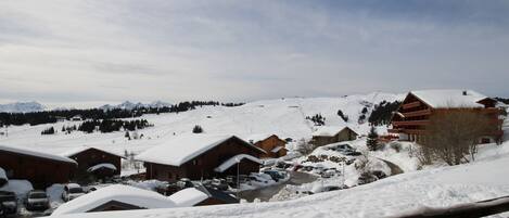A snow-covered village with traditional wooden buildings, a ski slope in the background, and a clear sky.