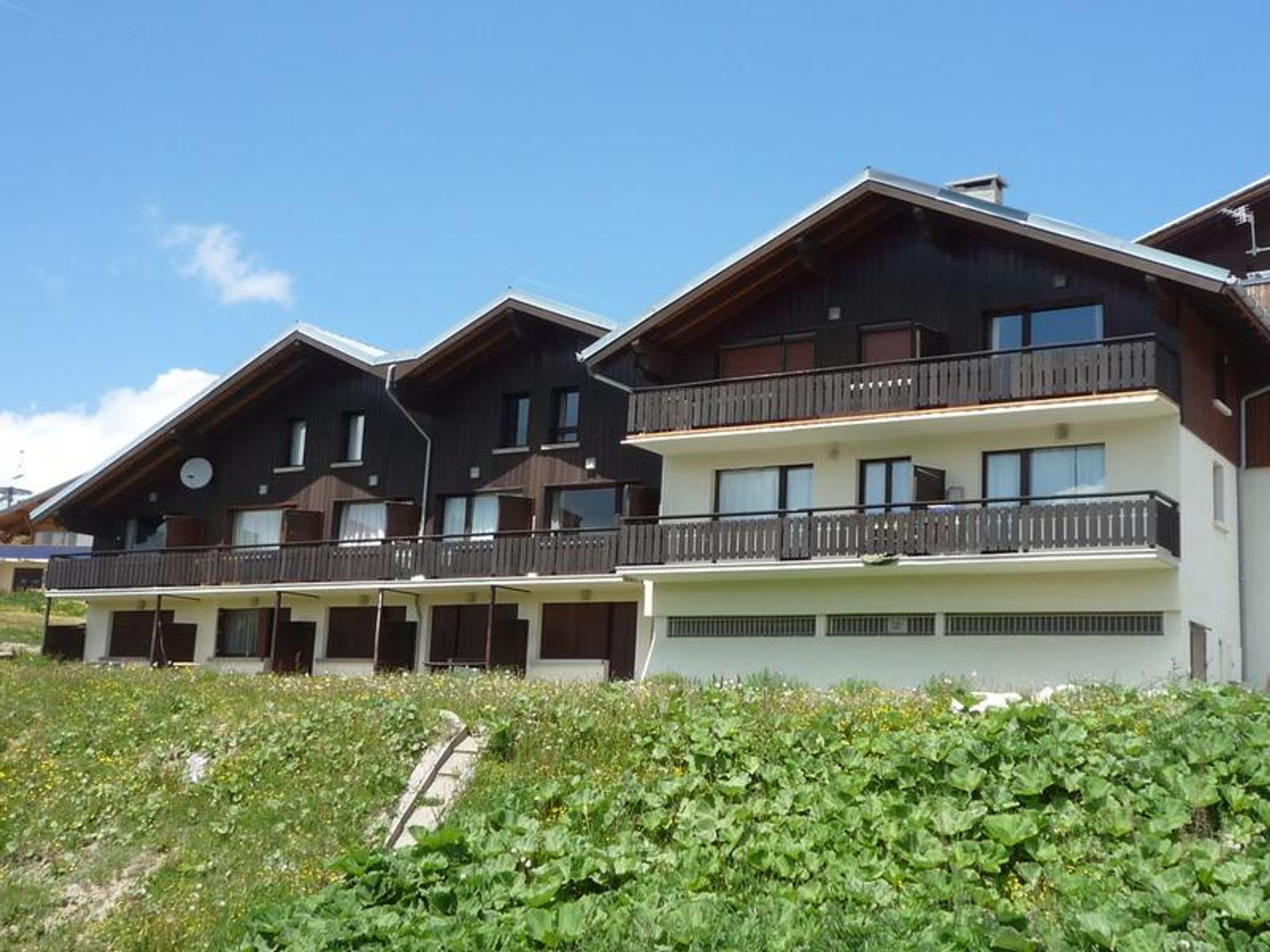 A multi-story building with balconies, a clear sky, and a grassy area in front.