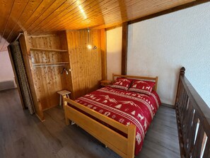A wooden-framed bed with a red patterned bedspread in a room with wooden walls and a sloped ceiling.