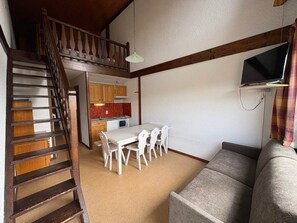 Ein kompakter Wohnraum mit Treppe, einem Essbereich mit weißen Stühlen, einer Couch und einer Küche mit Holzschränken und einer roten Spritzschutzwand.