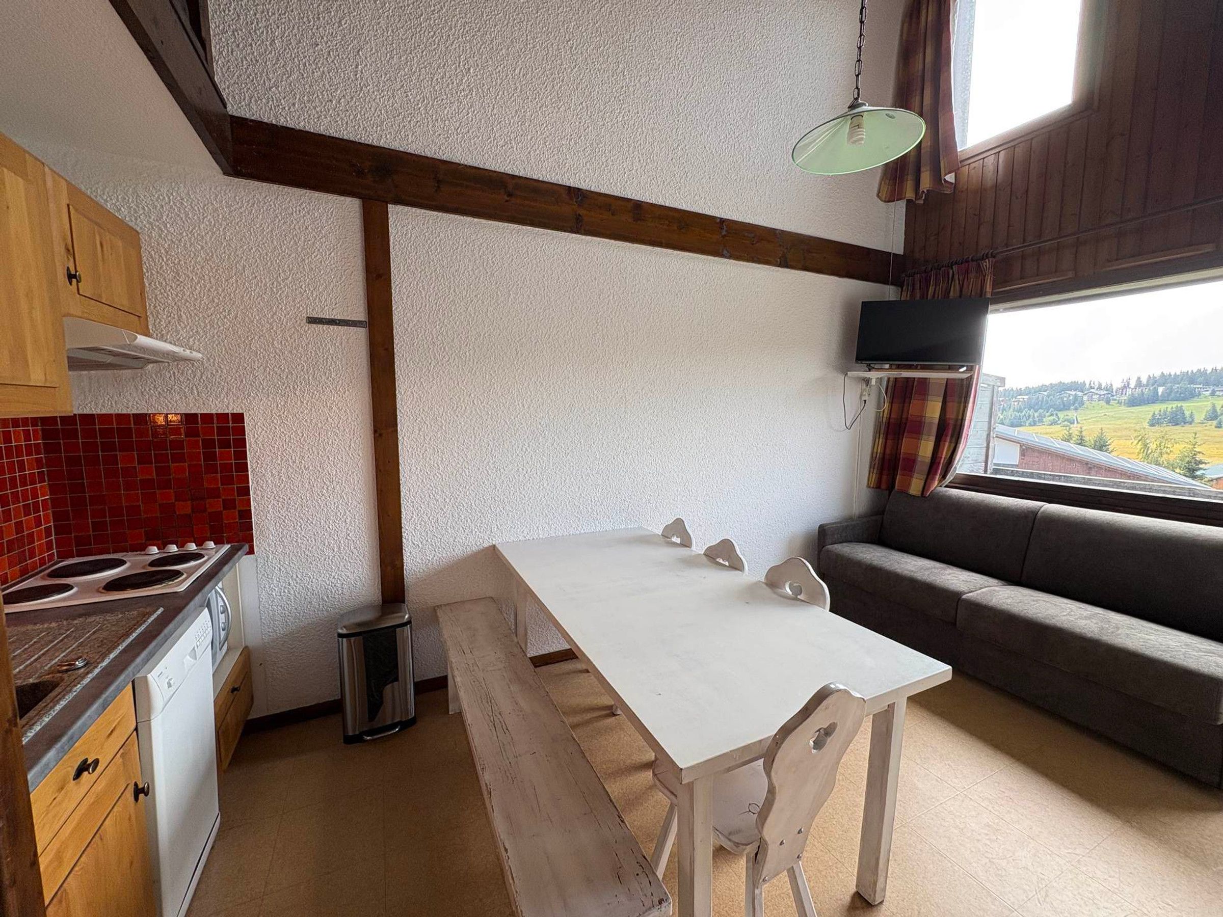 A kitchen with a white table and bench, wooden cabinets, a stove, and a window with a view of a landscape.