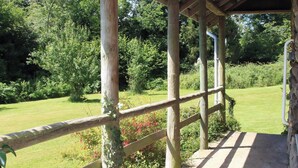 En træpergola med metalgelænder med udsigt over en græsplæne med træer og buske.