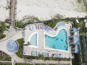 Vue aérienne d’un complexe hôtelier doté d’une grande piscine, de chaises longues et d’une zone de plage.