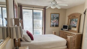 A bedroom with a bed, a bedside table, a lamp, a dresser, a ceiling fan, a window with curtains, and a painting on the wall. - 14th Floor End Unit w/ Wraparound Balcony (Orange Beach)