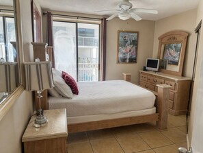 A bedroom with a bed, a bedside table, a lamp, a dresser, a ceiling fan, a window with curtains, and a painting on the wall. - 14th Floor End Unit w/ Wraparound Balcony (Orange Beach)